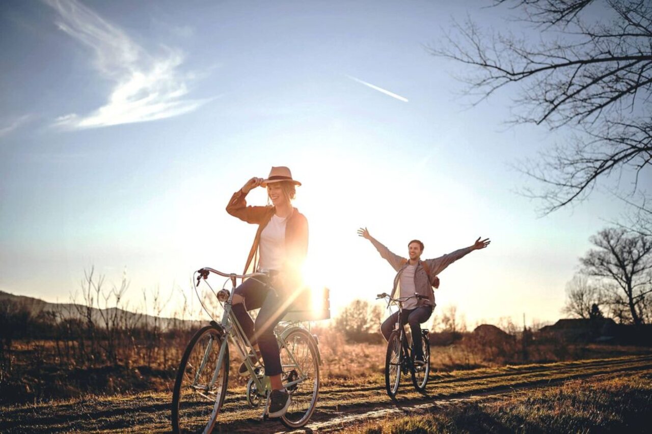 Zwei Menschen fahren bei Sonnenuntergang jubelnd Fahrrad